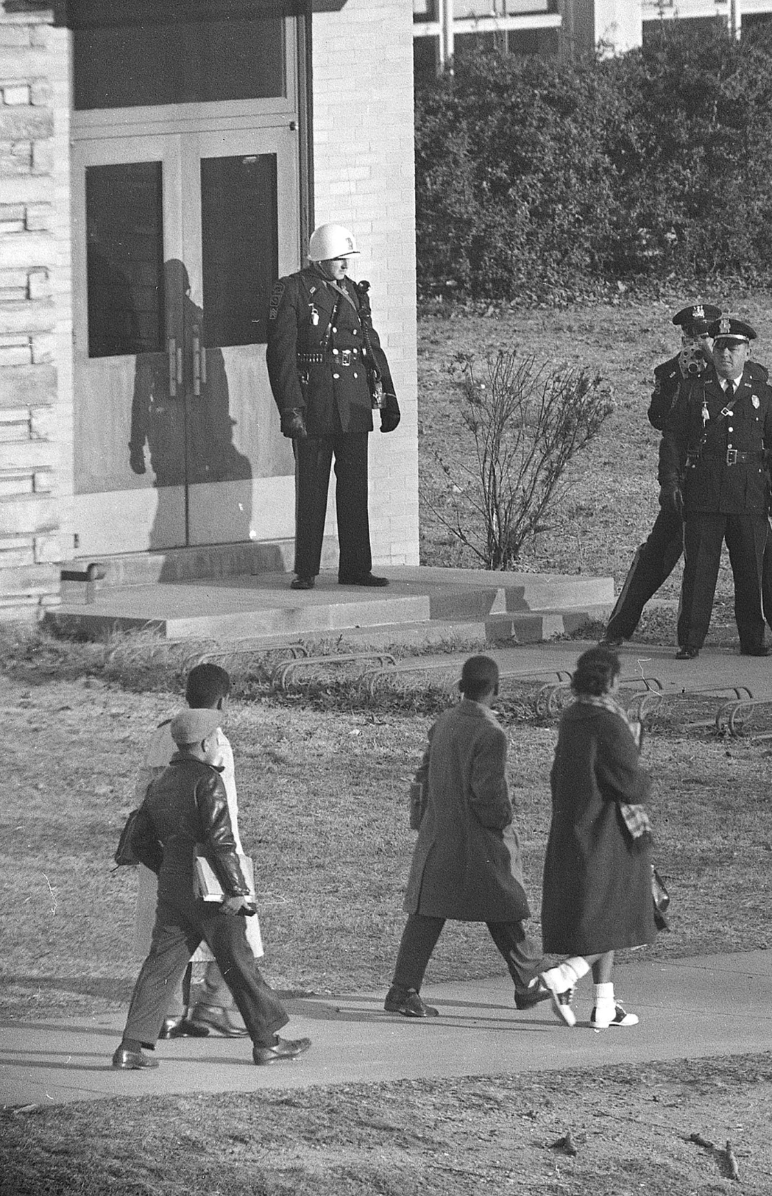 Three police officers stand at the entrance to Stratford Jr. High School as the four black students enrolled in the previously all-white school arrive for classes in Arlington, Va., on Feb. 3, 1959. One of the officers records the scene with a movie camera. Approaching the entrance are, left to right, Lance Newman, 13, Ronald Deskins, 12, Michael Jones, 12, and Gloria Thompson, 12. (AP Photo)